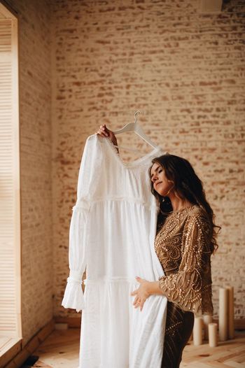 Woman holding wedding dress while standing against wall