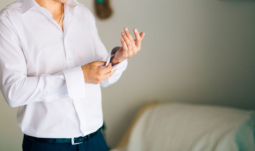 Midsection of woman holding mobile phone while standing on bed
