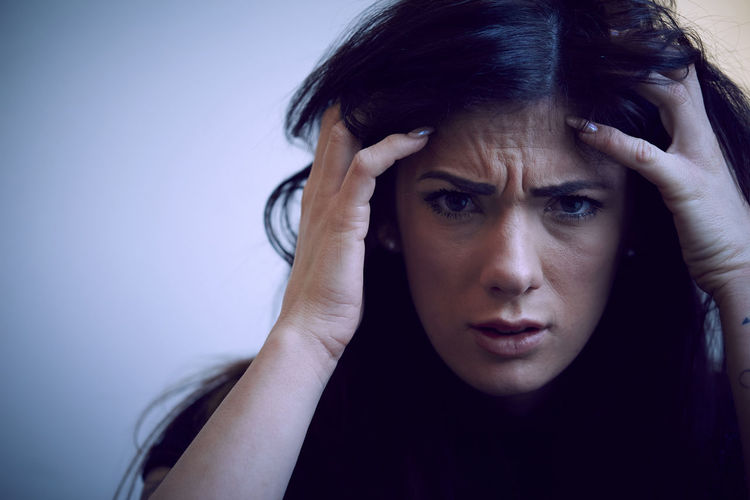 Portrait of depressed woman with hands in hair against wall