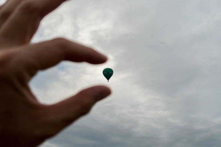 Low angle view of hand holding balloons against sky