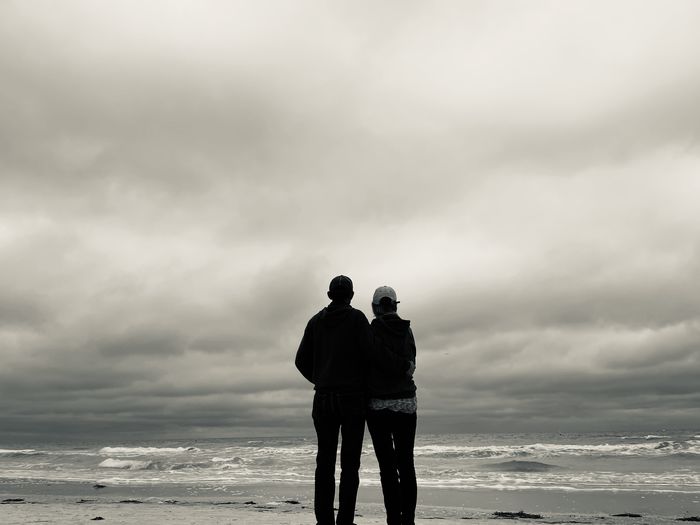 Rear view of senior couple silhouetted looking out over sea and stormy gray sky.  uncertain future