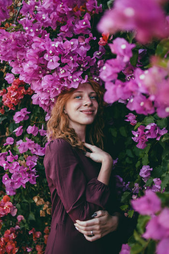 Portrait of smiling young woman standing by flowering plants
