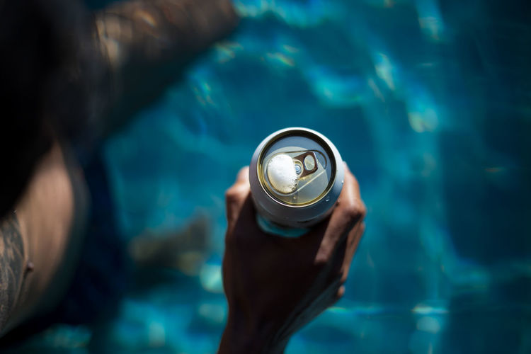 Selective focus white beer can in hand. man is soaking in the pool with an open beer can 