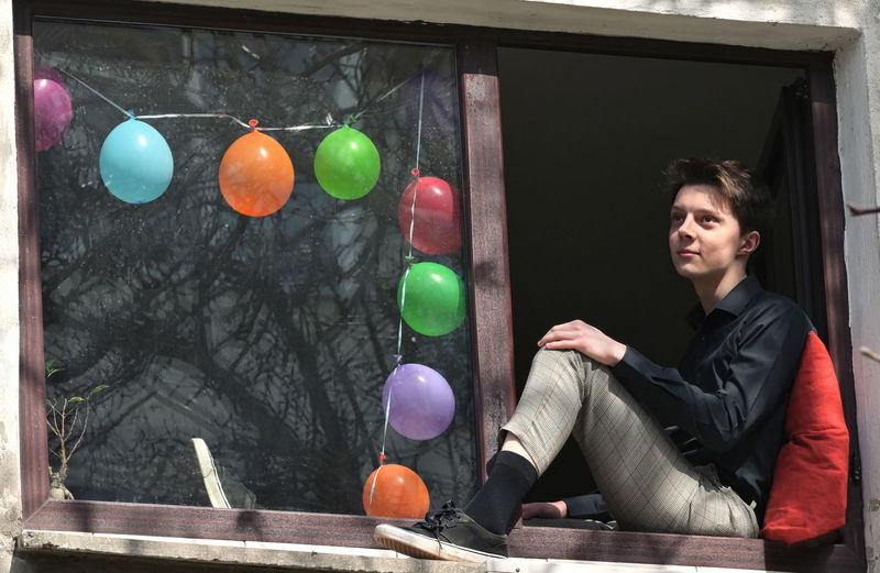 Thoughtful teenager sitting at window sill against multi colored balloons