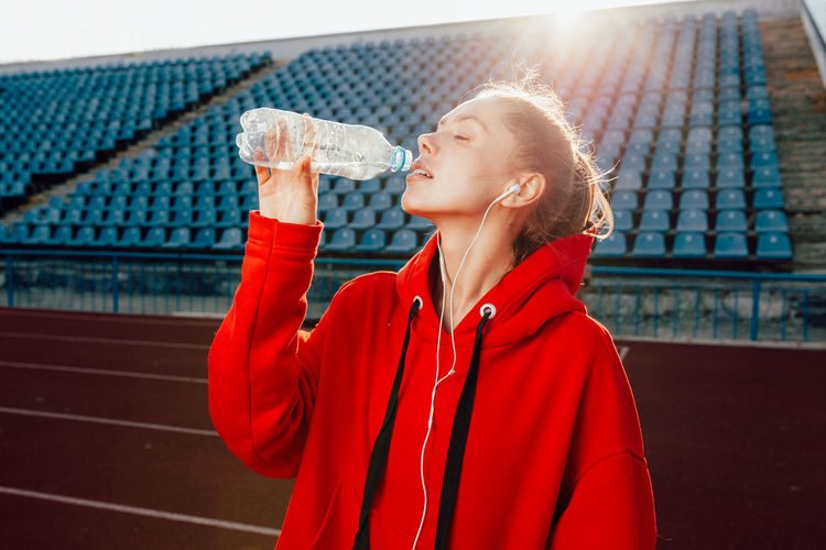 Female athlete drinking water while standing on running track