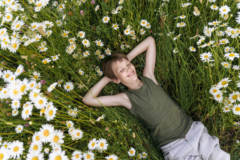 Smiling boy with hands behind head lying on chamomile plants in field