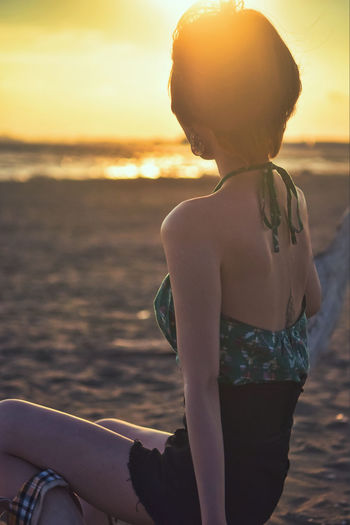 Rear view of woman sitting on beach during sunset