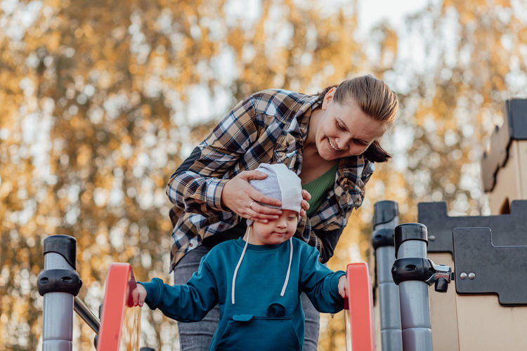 A boy, person with down syndrome walks in the park with his mother, spinning on the carousel