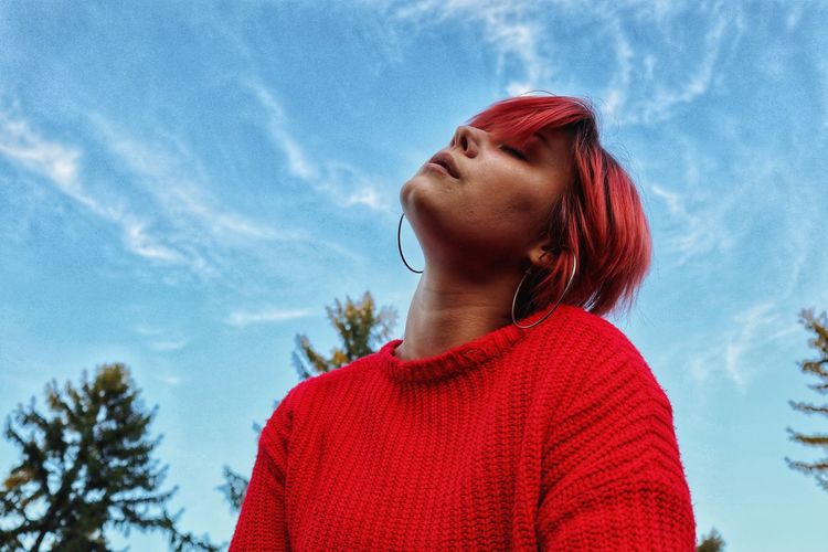 Low angle of young woman standing against sky