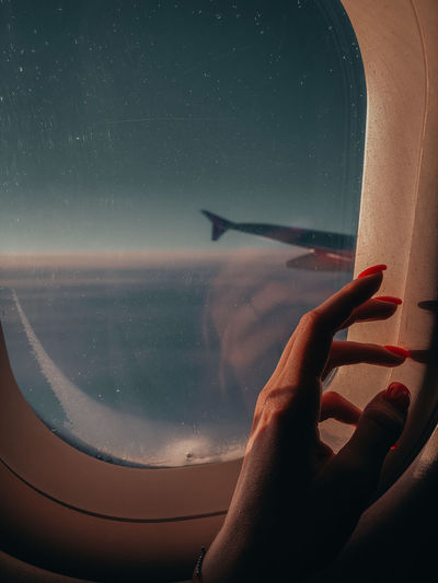 Aerial view of hand against sky seen through airplane window