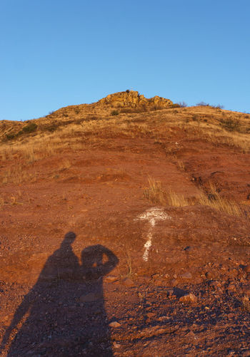 Shadow of man on rock formations against clear blue sky