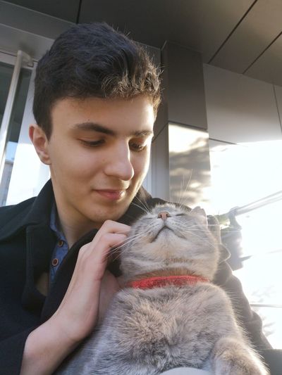 Young man holding cat while sitting outdoors