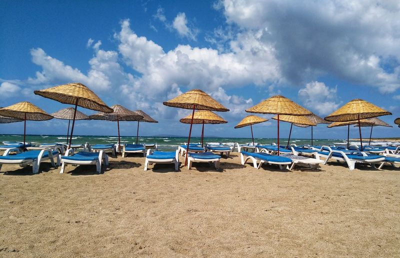 Lounge chairs and parasols on beach against sky
