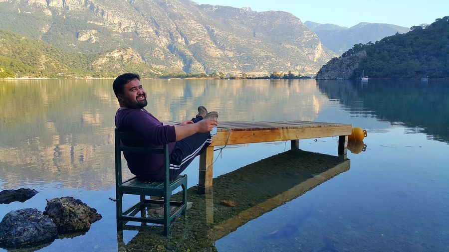 Portrait of smiling man sitting on chair in lake