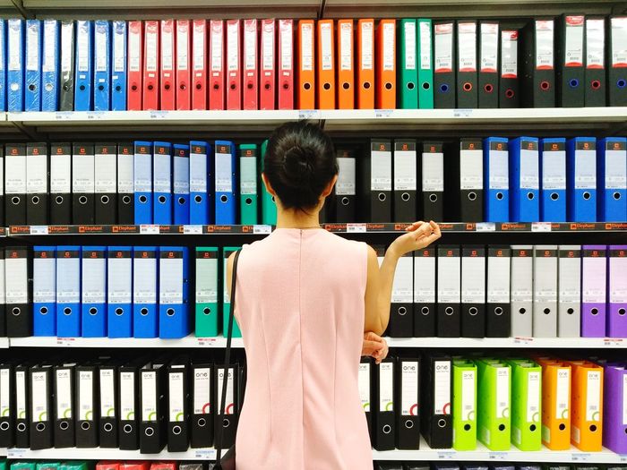 Rear view of woman standing against shelf at office
