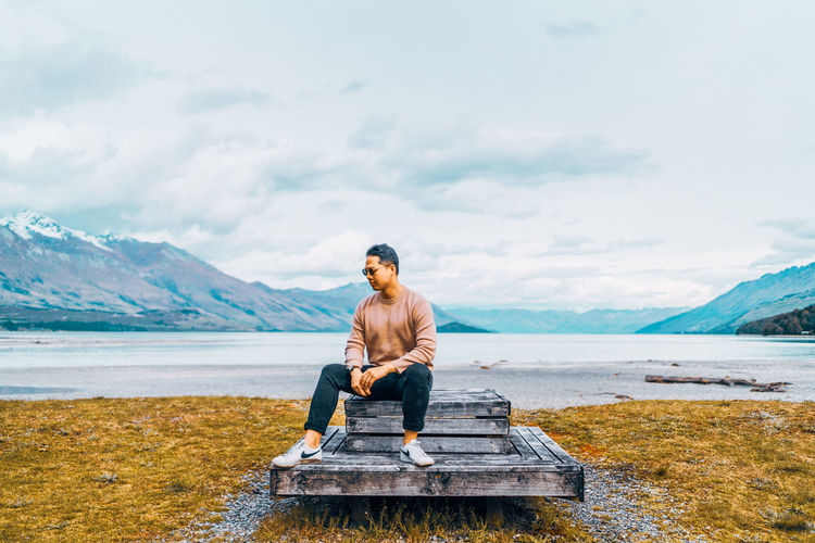 Full length of man sitting on lake against mountains