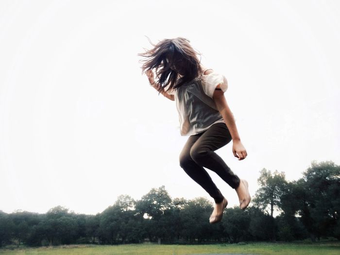 Low angle view of woman jumping against clear sky at park