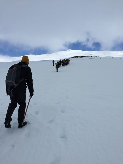Rear view of hikers climbing uphill against cloudy sky