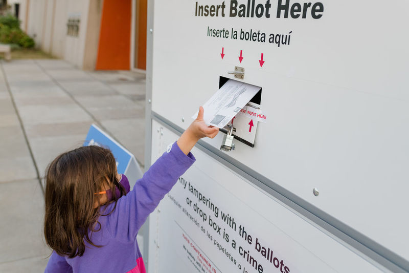 Little girl placing ballot in a drop box for absentee voting