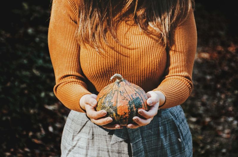 Midsection of woman holding pumpkin while standing on land
