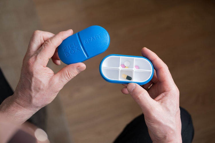 Man's hands are holding blue six day pill box with pills.