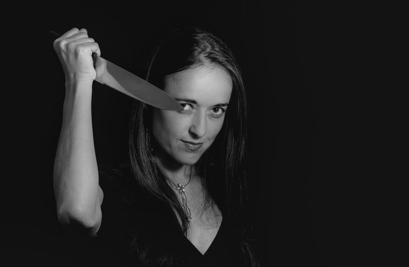 Portrait of young woman holding knife against black background