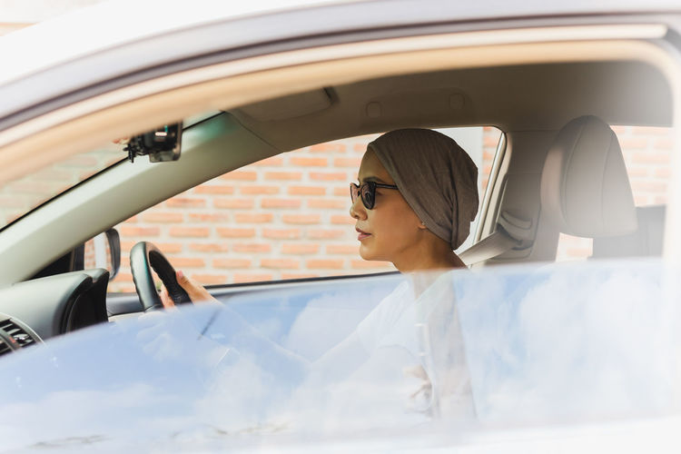 Asian woman wearing sunglasses driving a new car