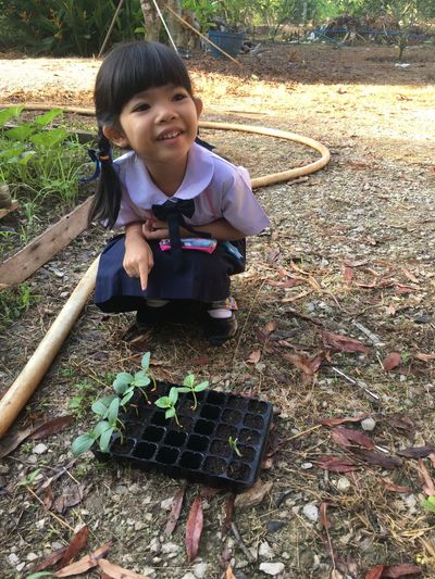 Happy girl crouching by seedling tray on field