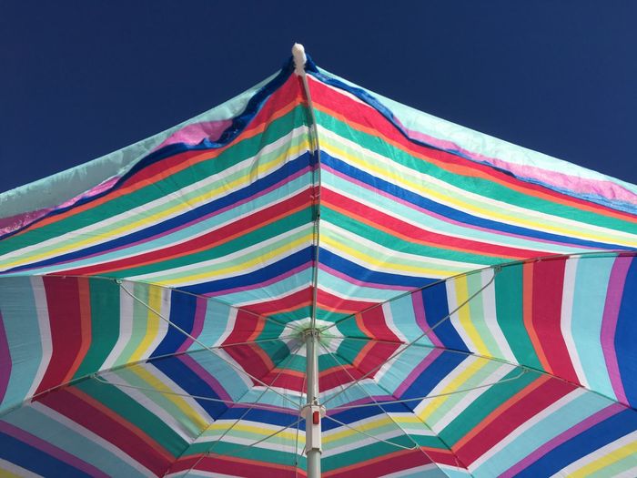Low angle view of multi colored umbrella against clear blue sky