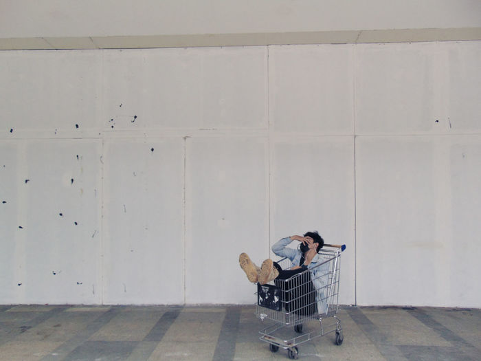 Man sitting in shopping cart against wall