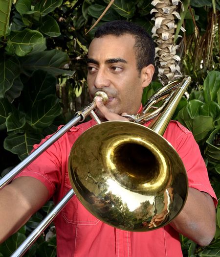 Mid adult man playing saxophone while standing against trees