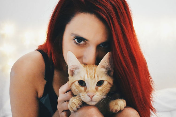 Close-up portrait of young woman holding cat while sitting on bed at home