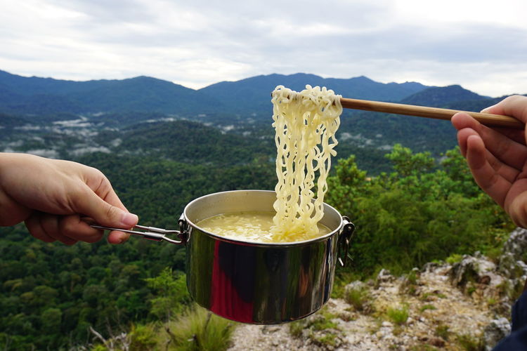 Midsection of person preparing food on mountain against sky