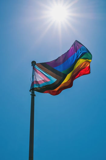 Low angle view of progress pride flag against sky