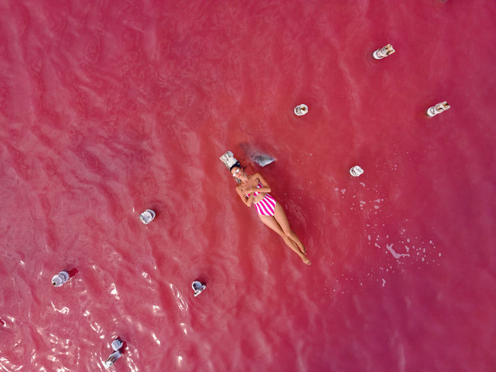 Woman in a pink bathing suit lies on a ruined wooden bridge in the middle of a pink lake in summer