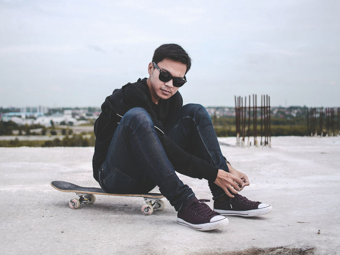 Portrait of man tying shoelace while sitting on skateboard at incomplete building