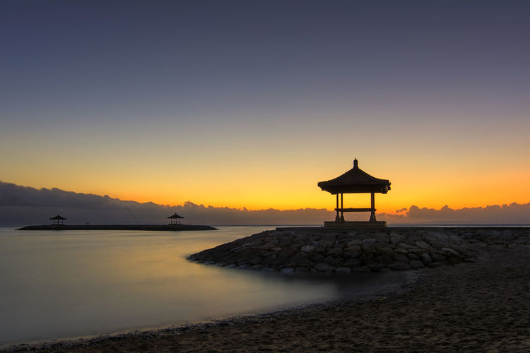 Silhouette cross on beach against sky during sunset