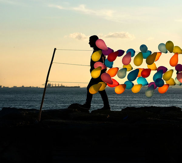 Man with balloons at beach during sunset