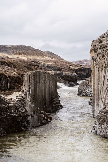 Spectacular scenery of river flowing through studlagil canyon with columnar basalt rock formations against overcast sky in iceland