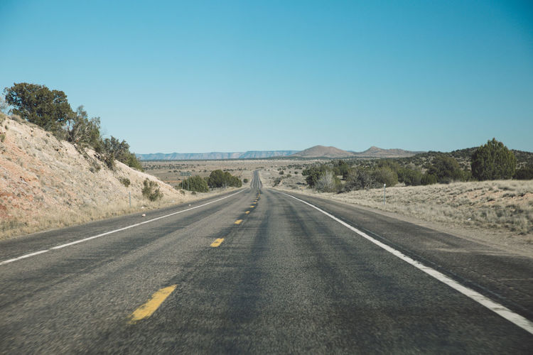 Empty country road passing through arid landscape against clear blue sky