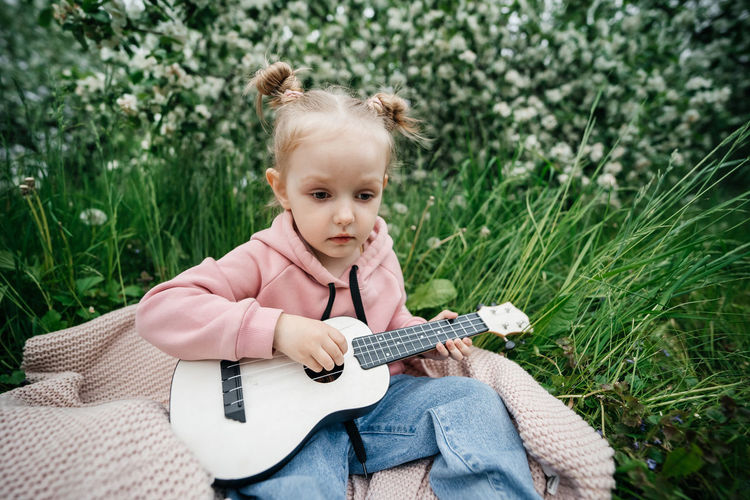 Little girl playing the ukulele in a blooming apple orchard in nature
