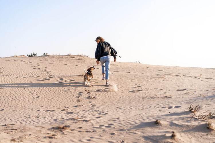 Rear view of woman with dog walking at beach