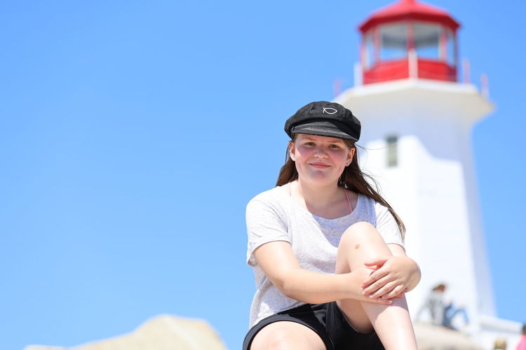 Portrait of smiling teenage girl sitting against lighthouse