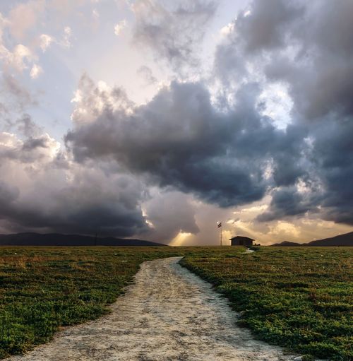 Dirt road amidst field against storm clouds