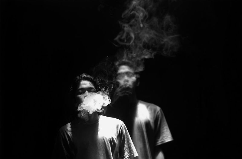 Young man smoking cigarette against black background