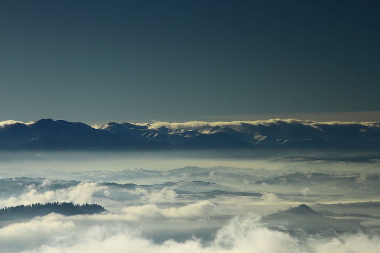 Scenic view of cloud covered mountains against clear sky at dusk