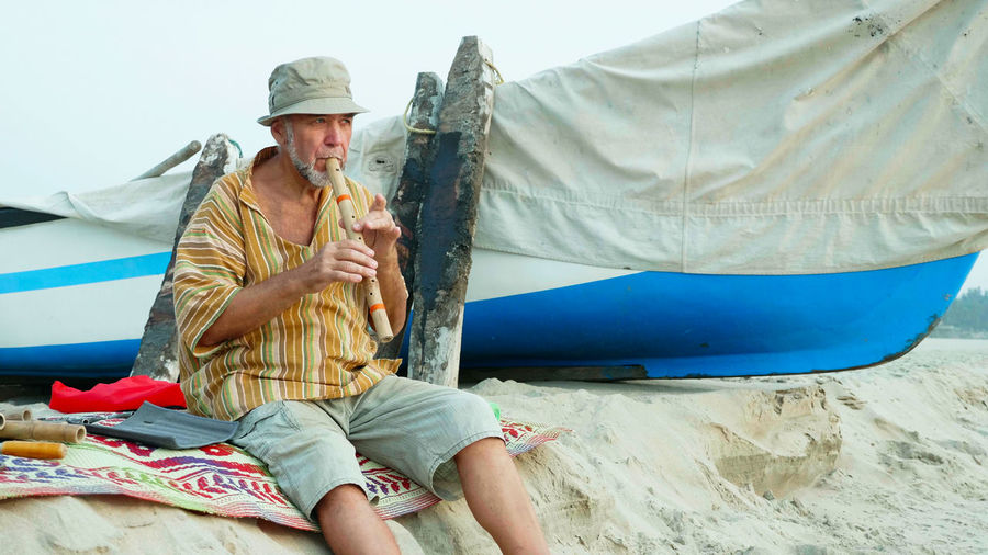 Man wearing hat playing flute sitting on beach