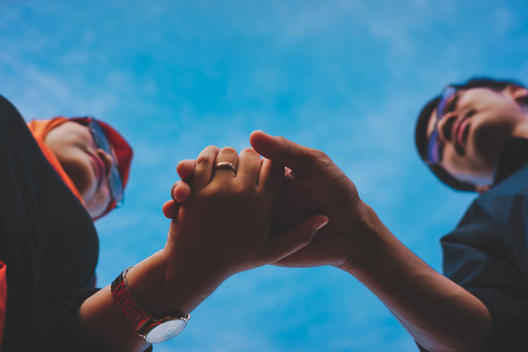 Low angle view of people hands against blue sky