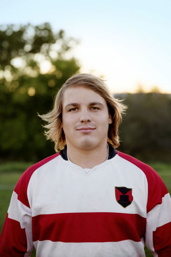Confident rugby player standing on field against sky