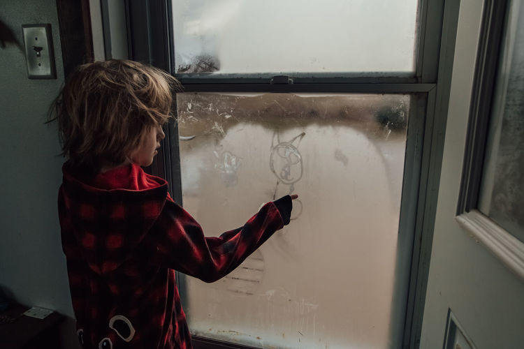 Little boy drawing a picture on the window condensation